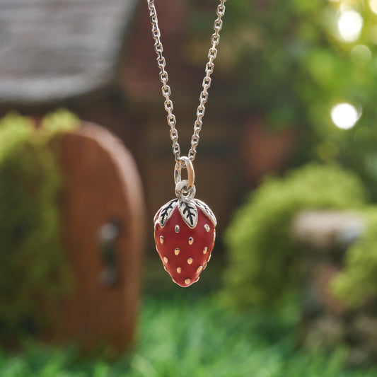 Hand-painted red enamel strawberry necklace front view with silver leaf cap in garden setting