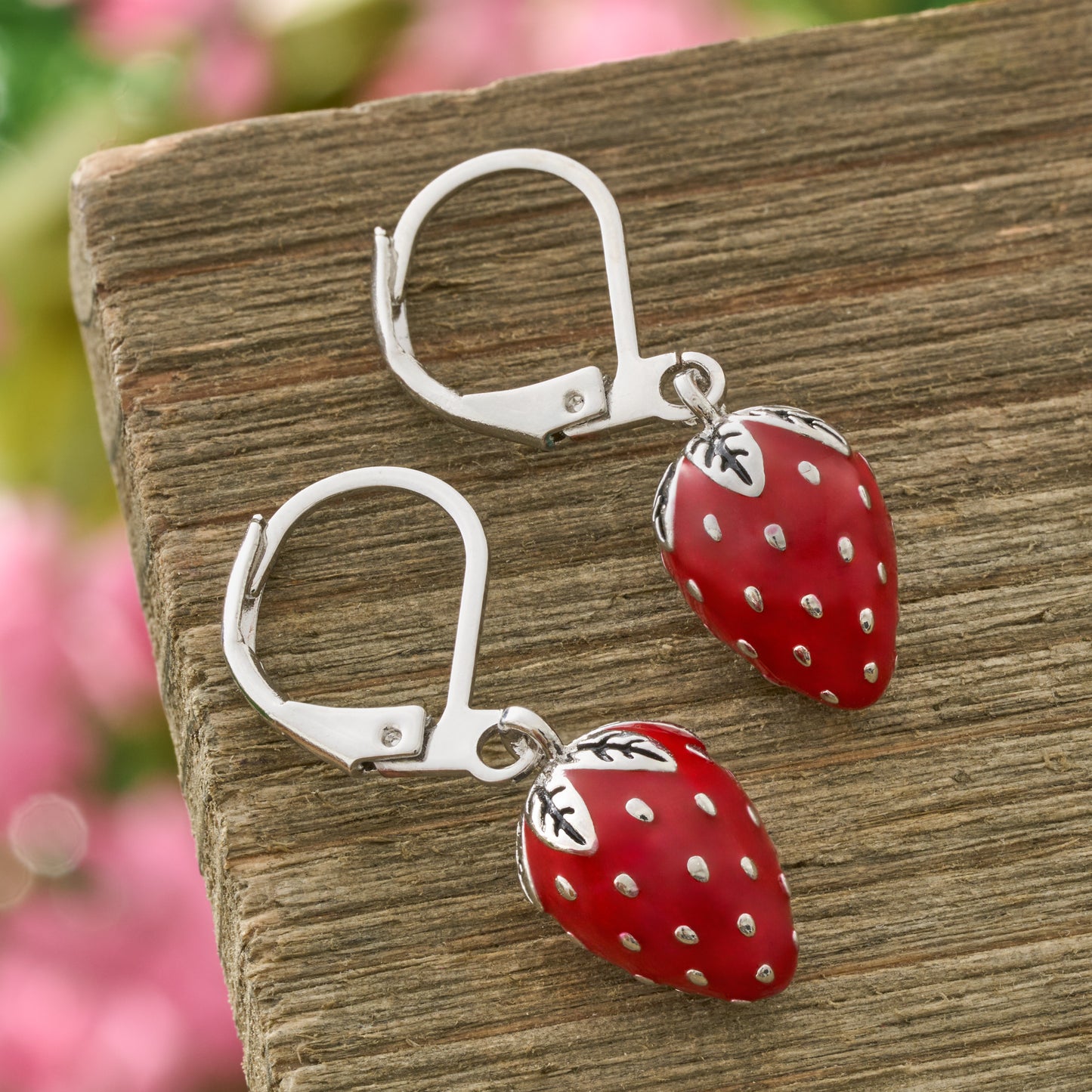 Hand-painted red enamel strawberry leverback earrings on rustic wood background