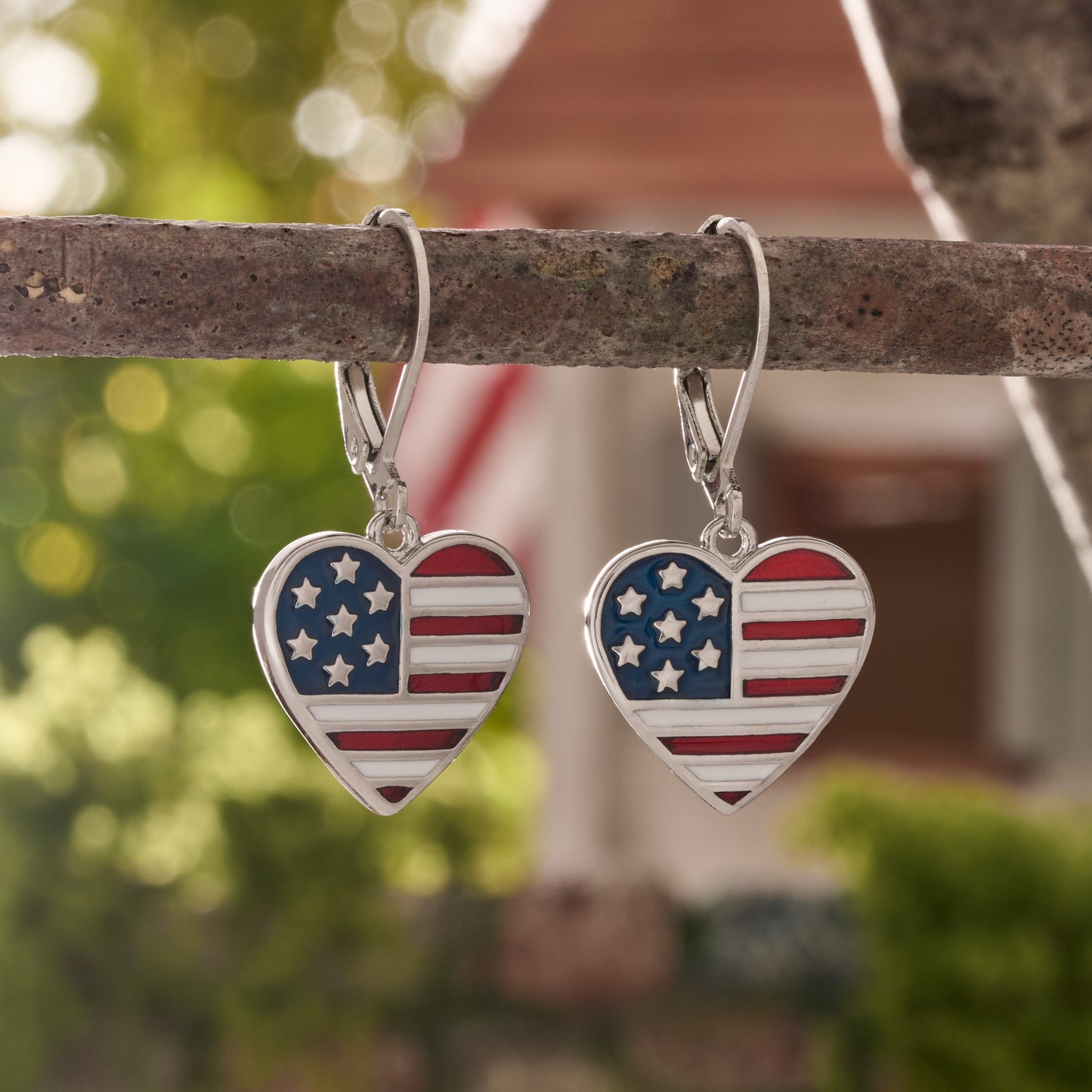 American flag heart leverback earrings with red white and blue enamel hanging from branch in front of home


