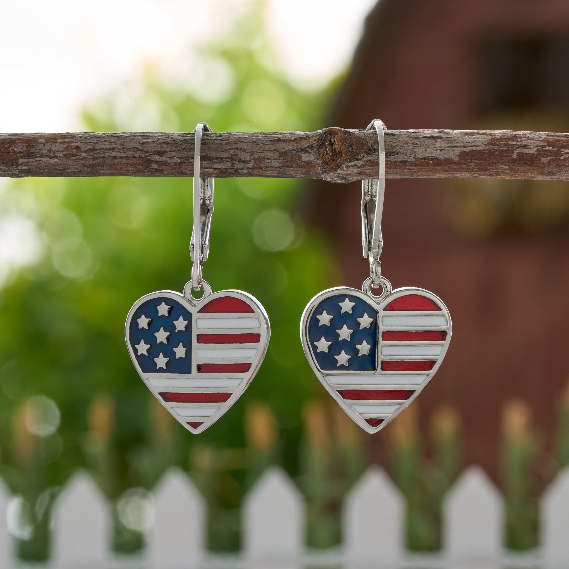Patriotic heart leverback earrings with American flag enamel by white picket fence for July 4th

