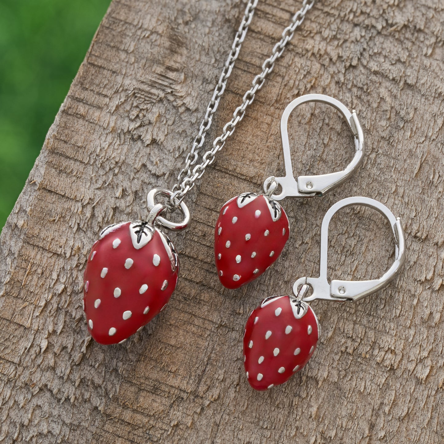 Hand-painted red enamel strawberry leverback earrings with matching necklace on rustic wood

